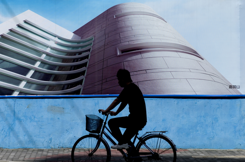 A man rides a bicycle past billboards erected around a real estate building site in Shanghai, 2010. (Photo: Philippe Lopez/AFP/Getty Images)